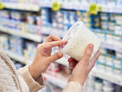 Nahaufnahme: Eine Frau hält im Supermarkt eine Plastikdose vor einem Kühlregal in der Hand