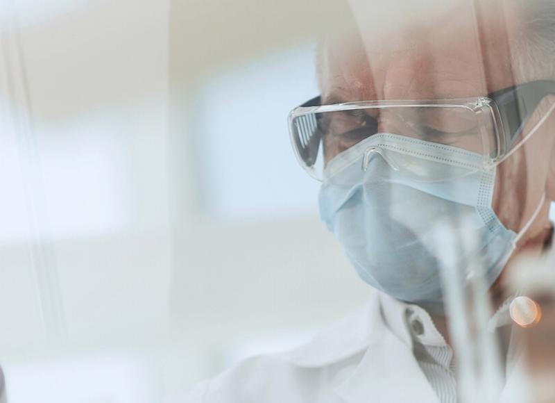 Mann im Labor-kittel mit Mundschutz, Schutzbrille, Handschuhen und PipetteK